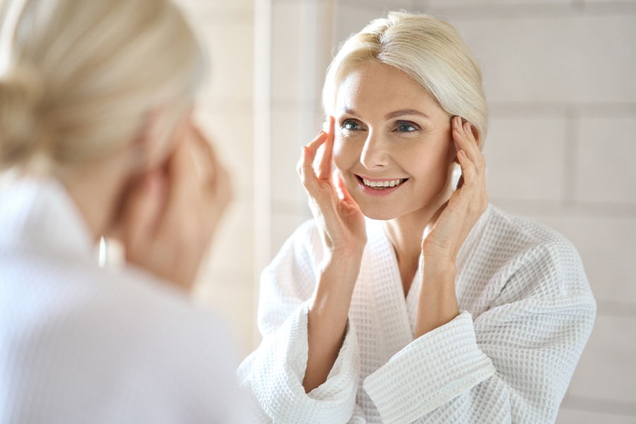 mature woman with flawless skin looking in mirror smiling